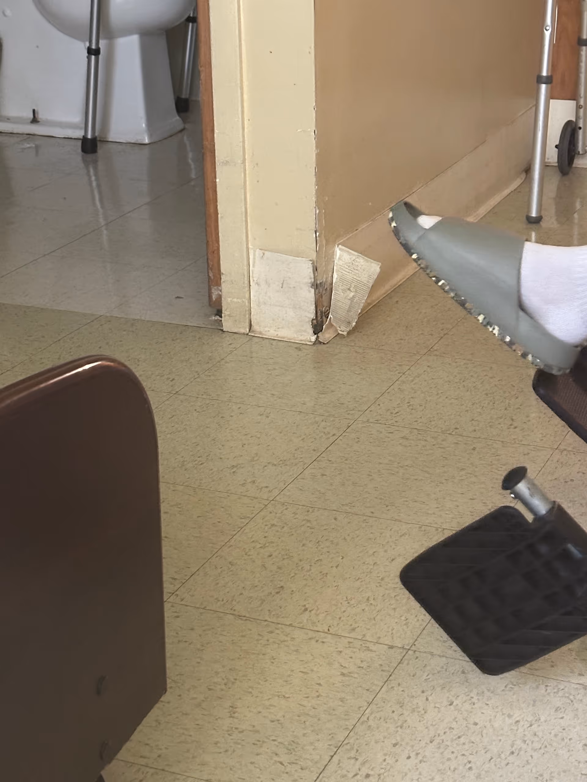 Interior facility hallway with a bathroom doorway, chipped baseboard, and a resident's socked foot.