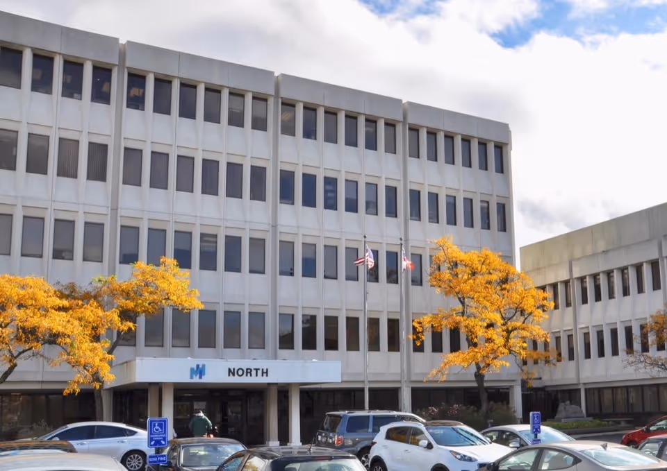 Exterior view of a large hospital building with a parking lot and fall trees.