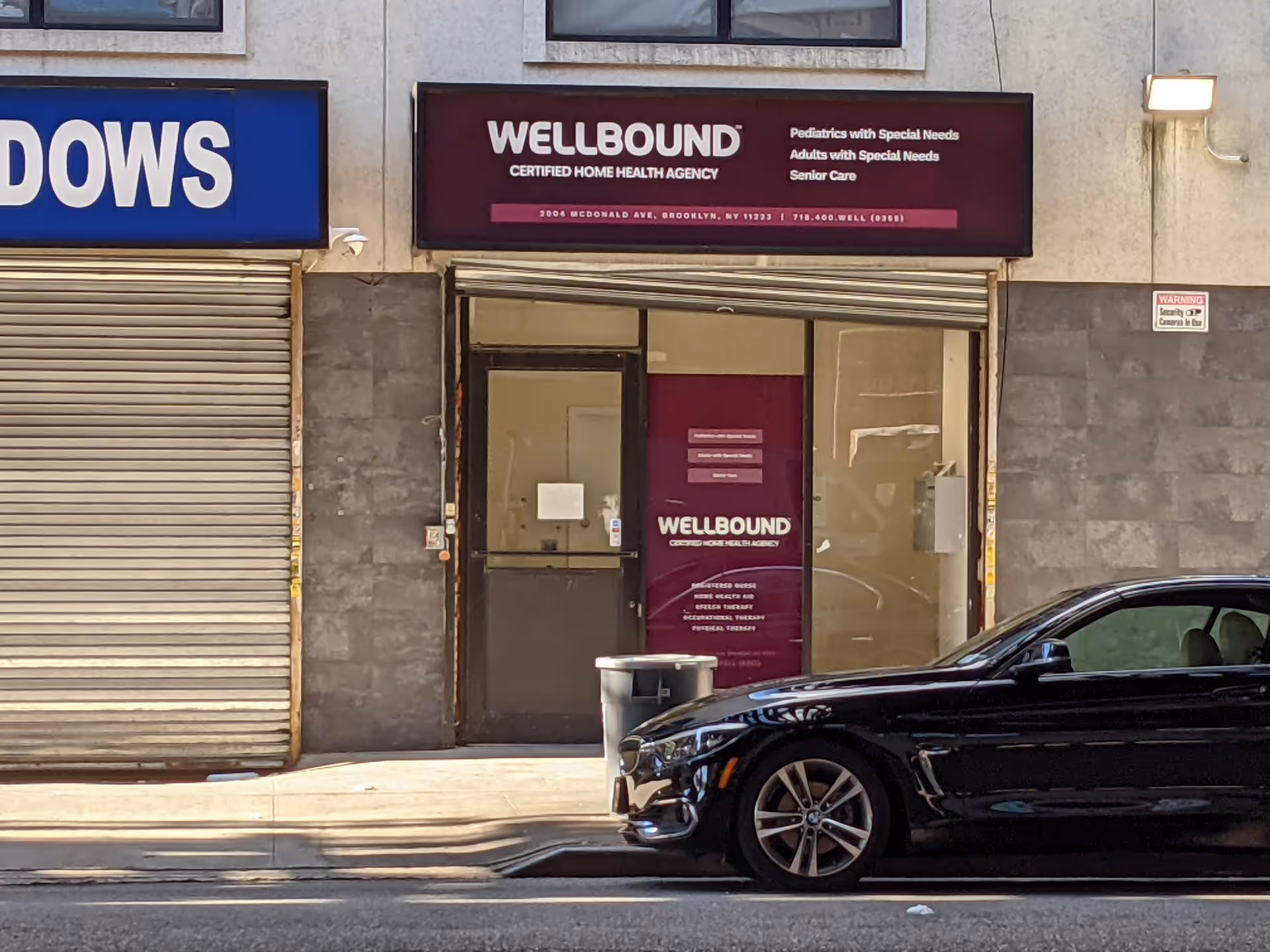 Urban storefront with Wellbound sign, glass door, and a black car parked outside.