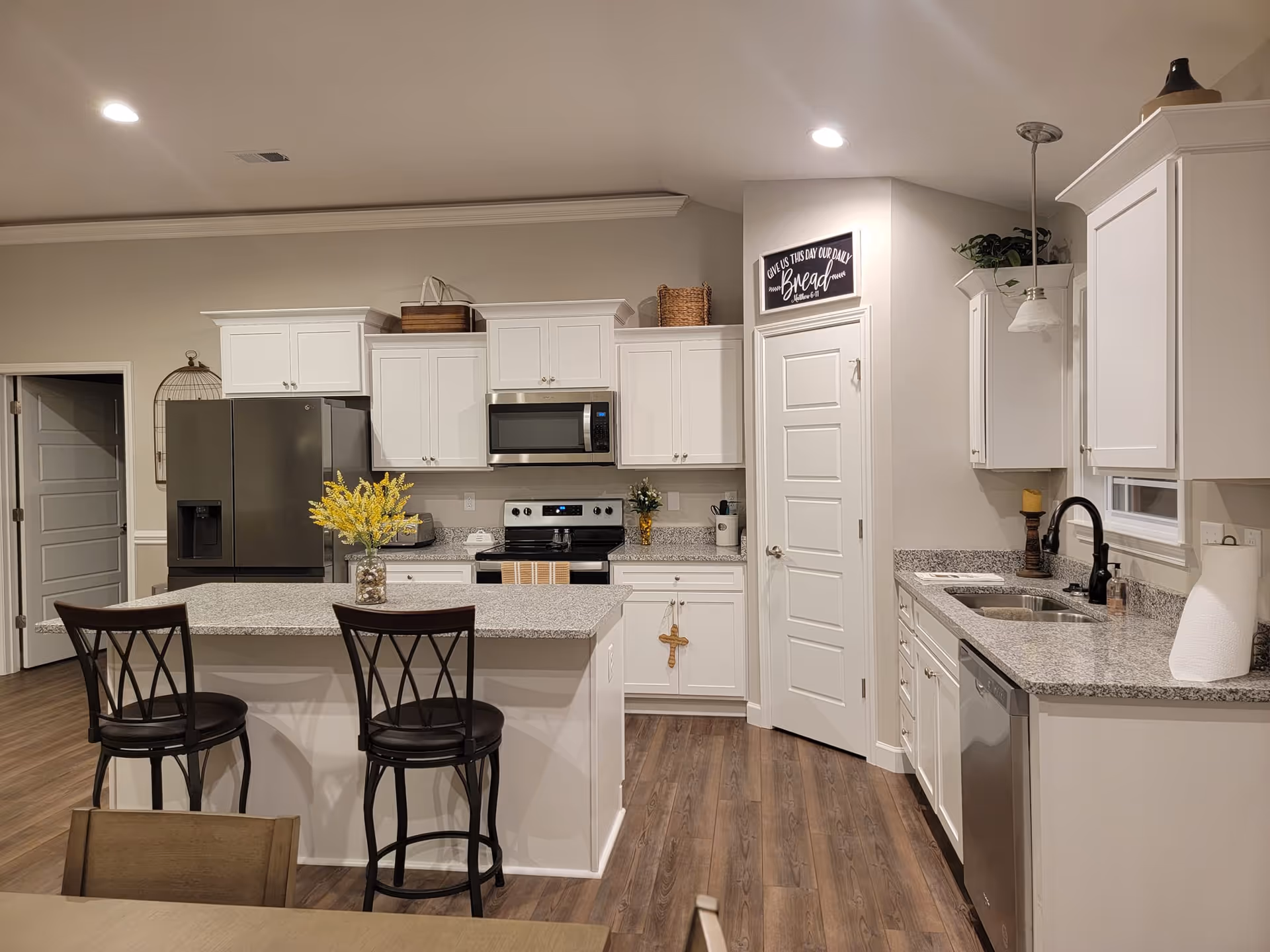 Bright white kitchen with island, granite countertops, and stainless steel appliances.