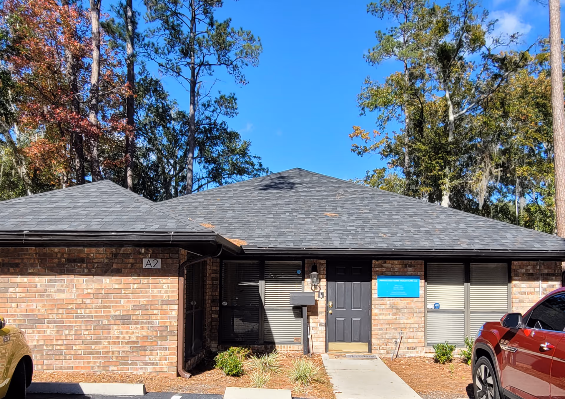 Brick, single-story facility entrance with a blue sign and parked cars outside.