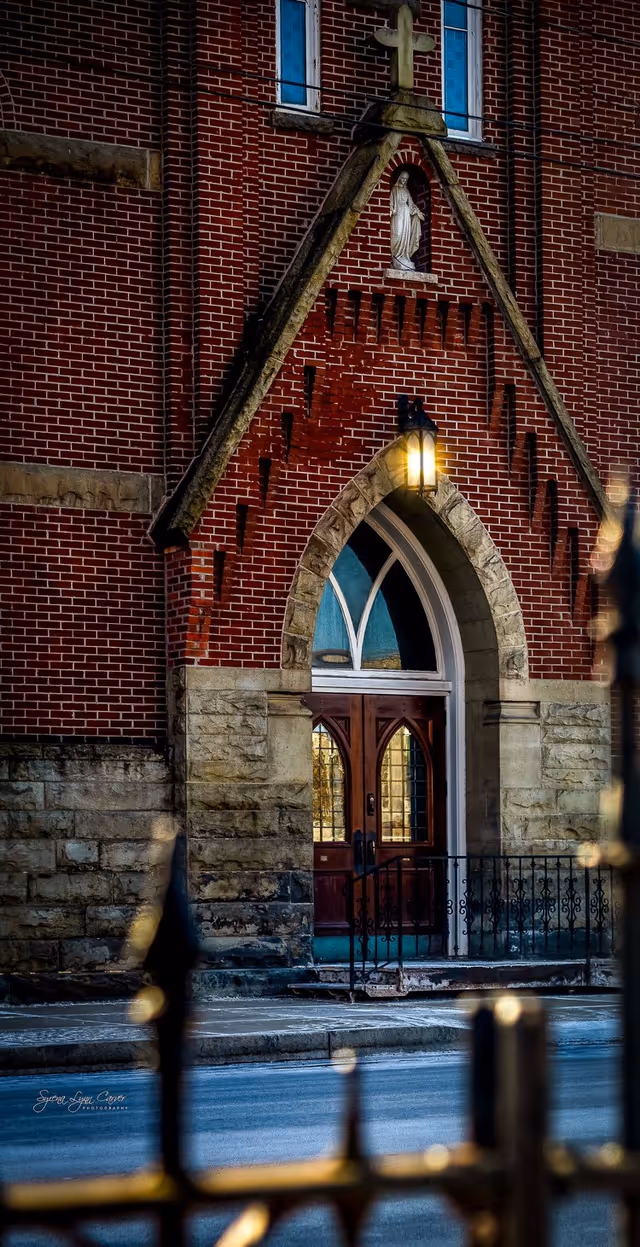 Brick building exterior with arched doorway, stone accents, and iron railing.