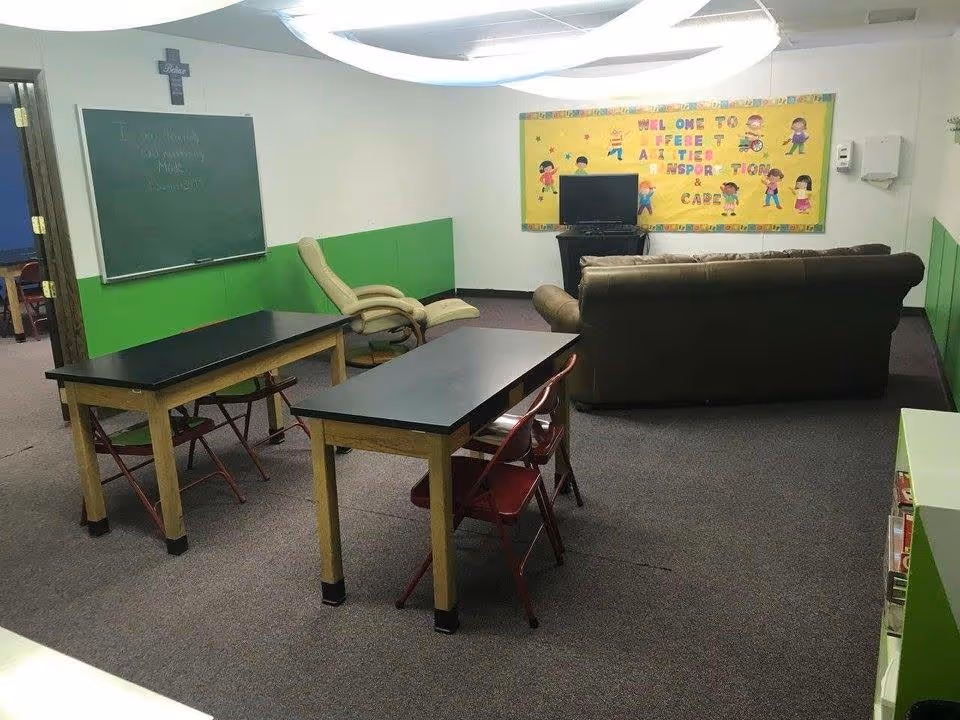 Activity room in a senior facility with tables, chairs, sofa, chalkboard, and TV.