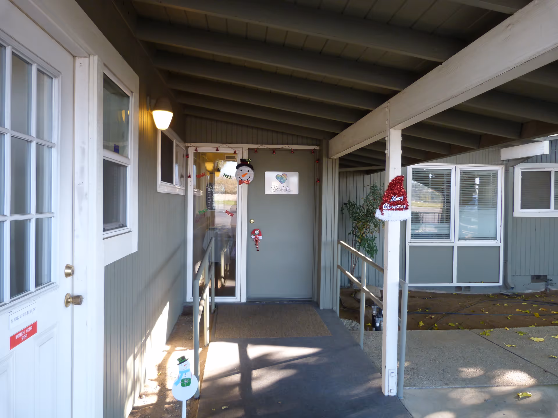 Covered exterior entrance area with doors, windows, and holiday decorations at a senior facility.