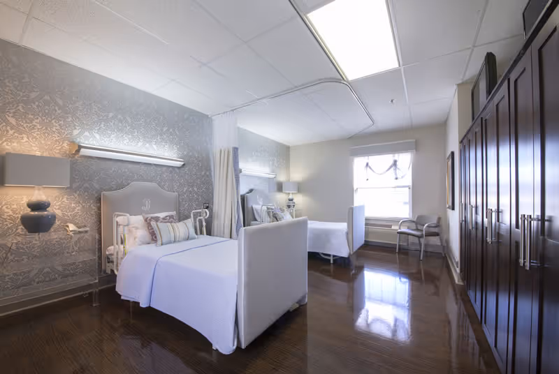 Two twin beds in a bright, patterned bedroom with closets, lamps, and seating.