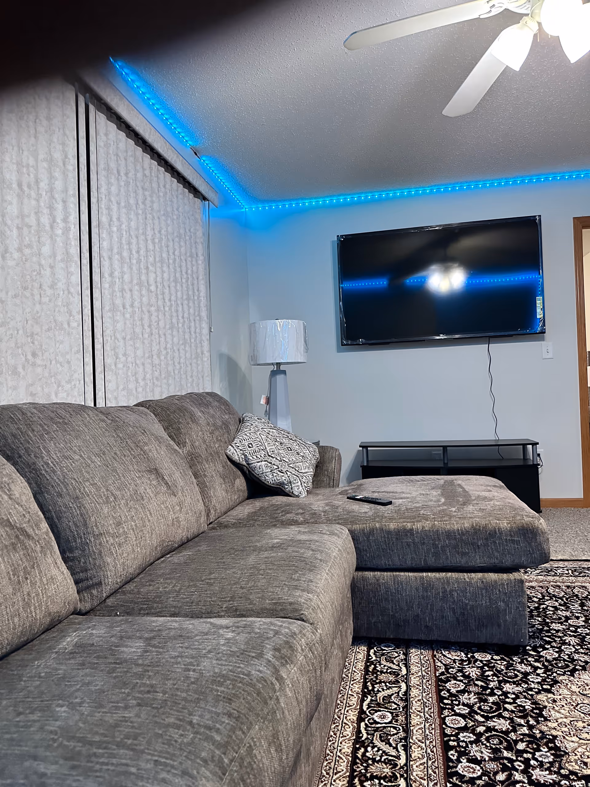 Grey sectional sofa facing a wall-mounted TV in a living room with blue LED strip lighting.