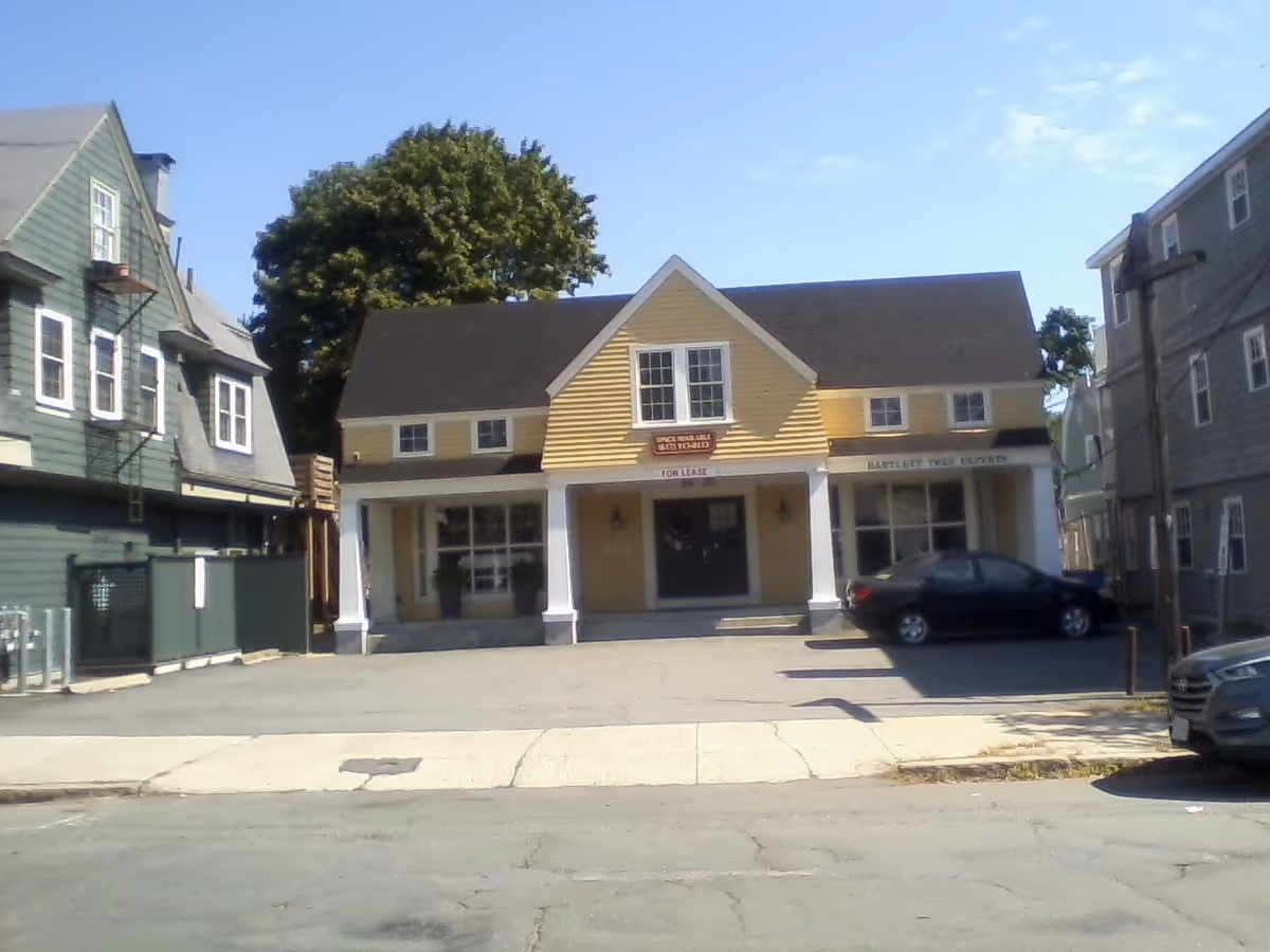 Yellow storefront with white columns on a street lined by neighboring houses.