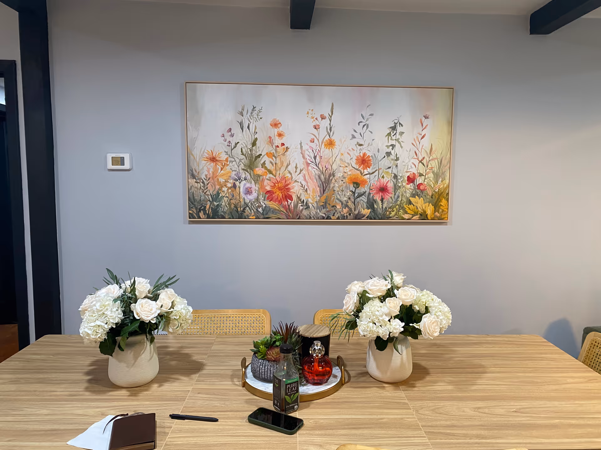 Wood dining table with white flower arrangements and a colorful wall painting.