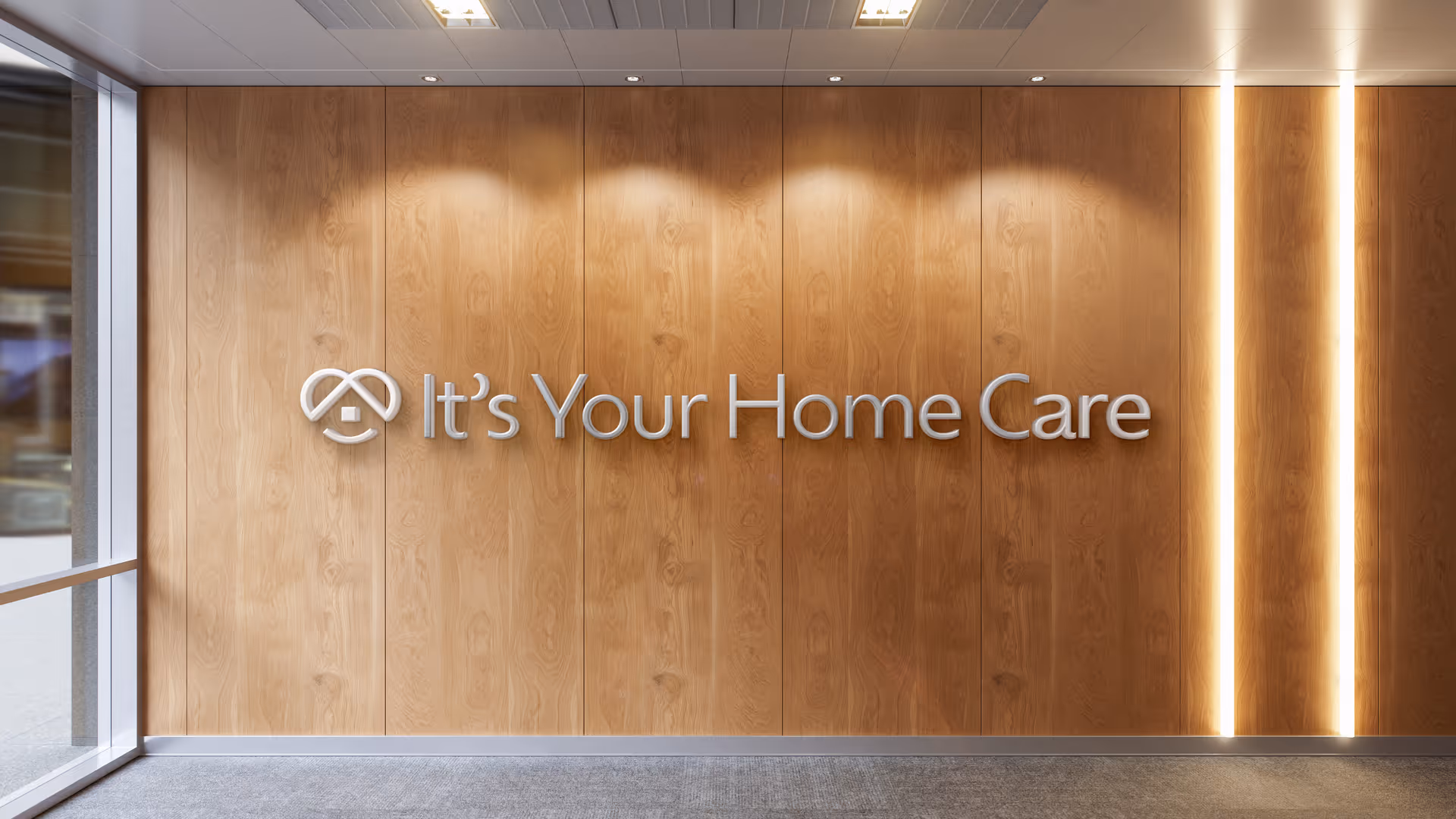 Wood-paneled wall with a silver sign reading It's Your Home Care in a lobby.