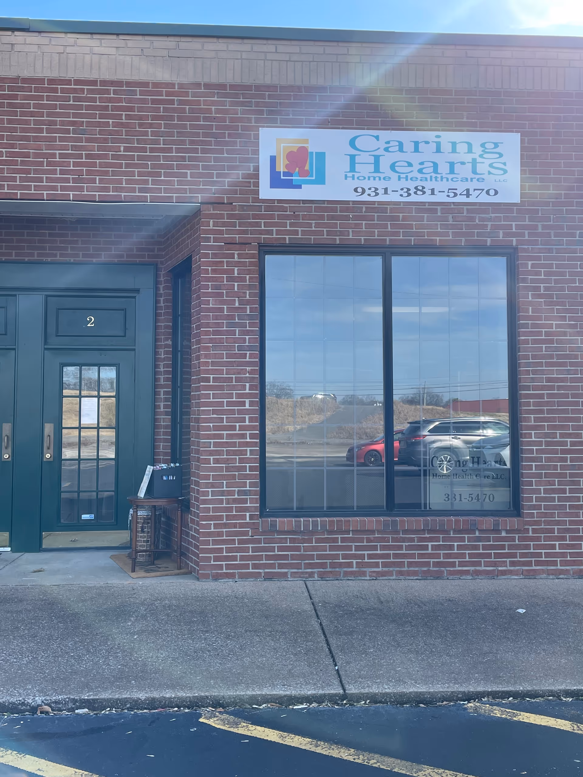 Brick storefront with Caring Hearts Home Healthcare sign, green door, and large window.