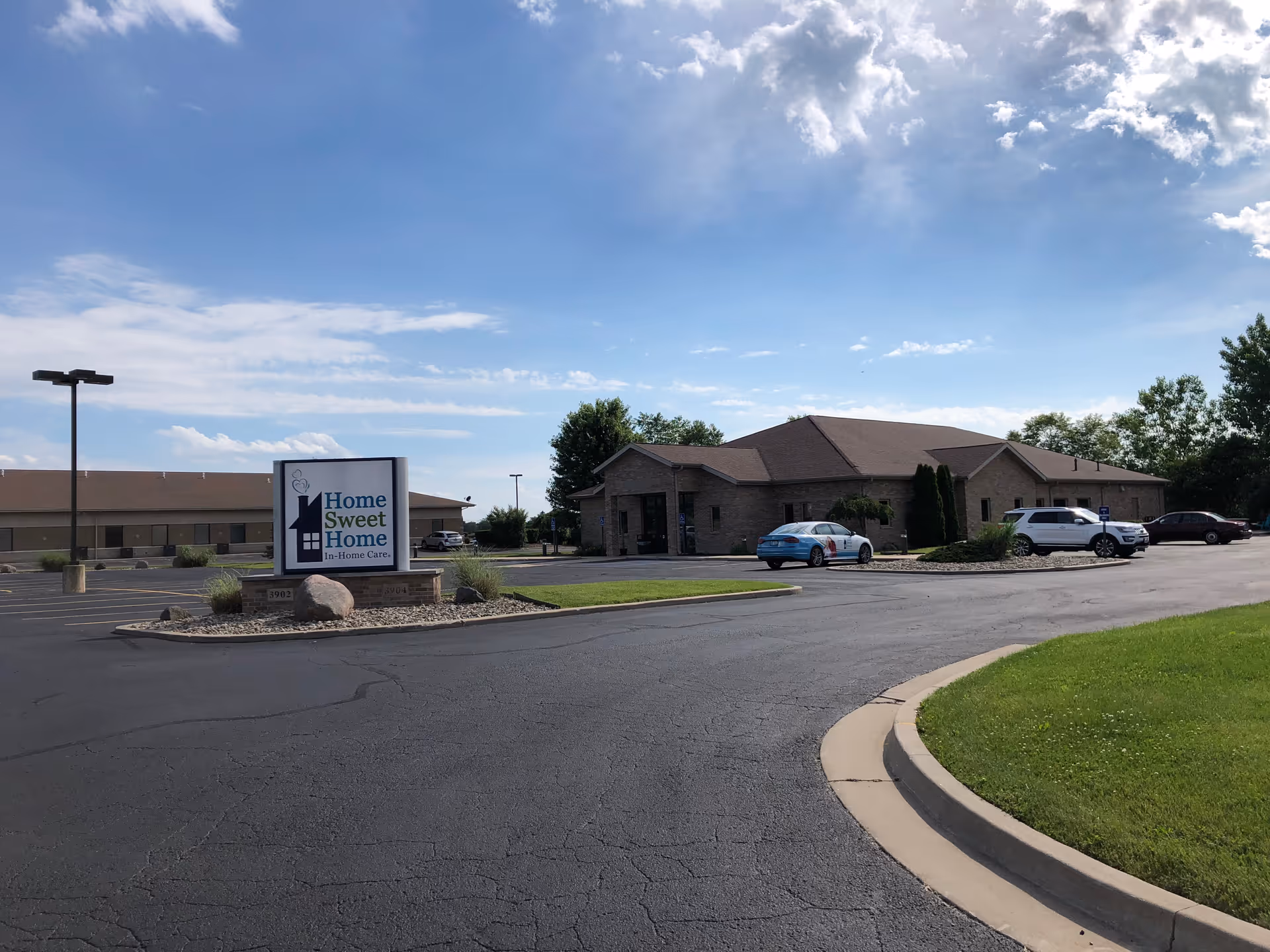 Exterior view of a brick senior care facility with a parking lot and sign.