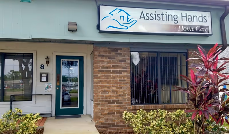 Front exterior of Assisting Hands Home Care storefront with door, window, and sign.