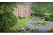 Brick senior living building with curved driveway, manicured lawn, and surrounding trees.
