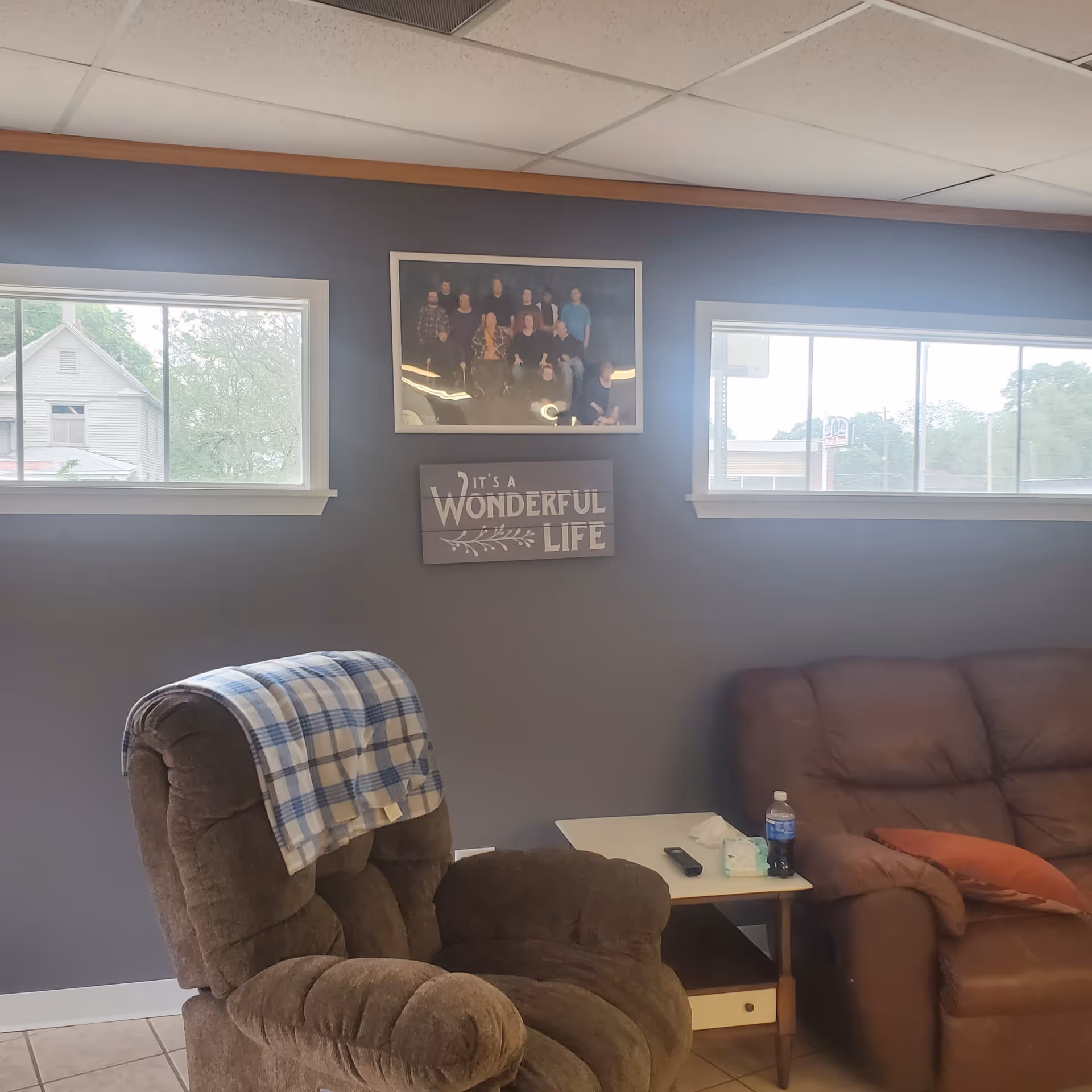 Cozy interior living area with recliner, sofa, wall art, and two windows.
