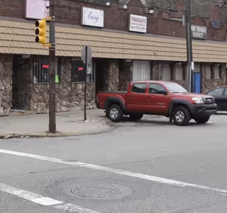 Red pickup truck parked on a city street in front of storefronts.