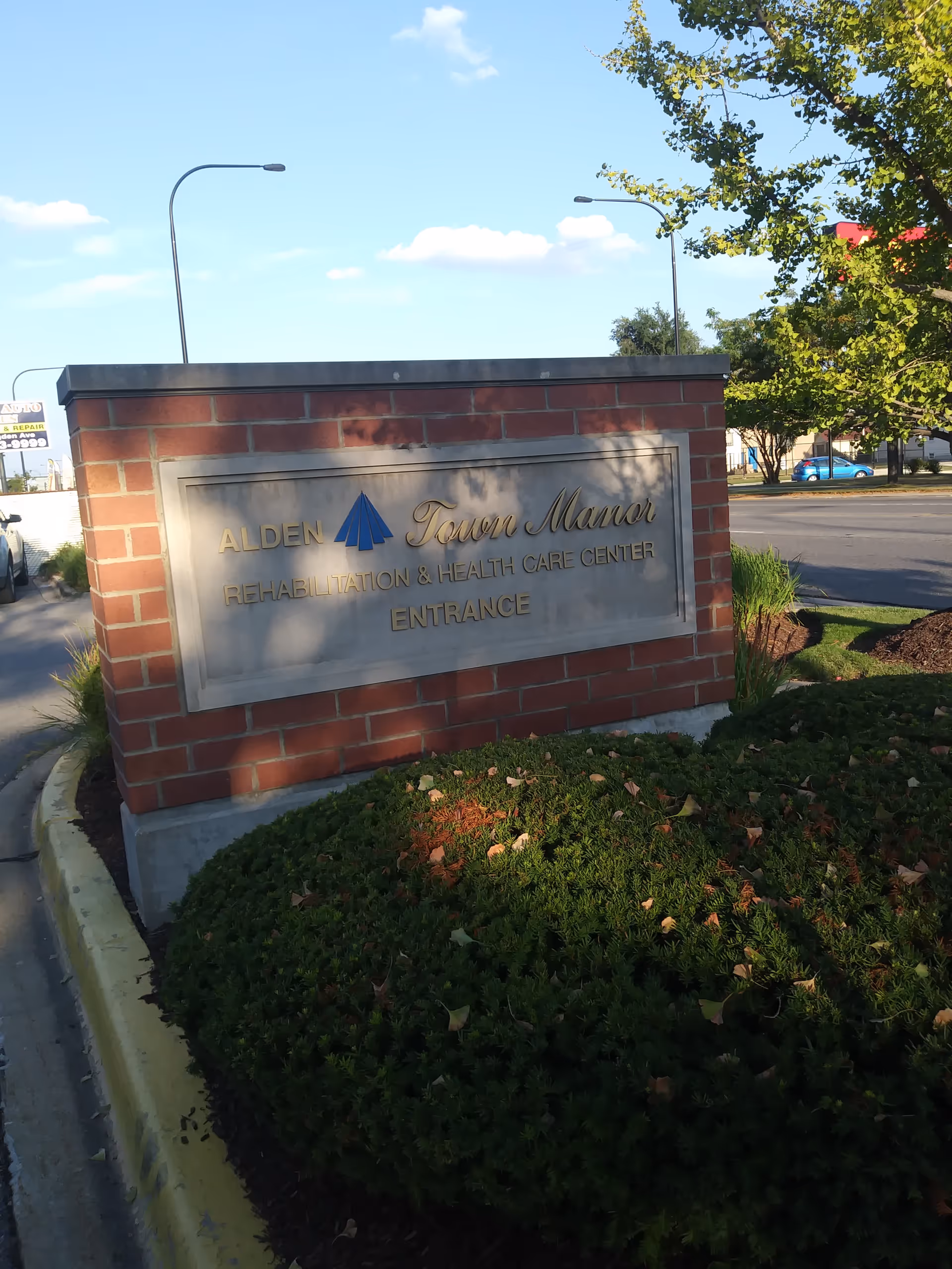 Brick sign with metal plaque displaying Alden Town Manor Rehabilitation and Health Care Center entrance.