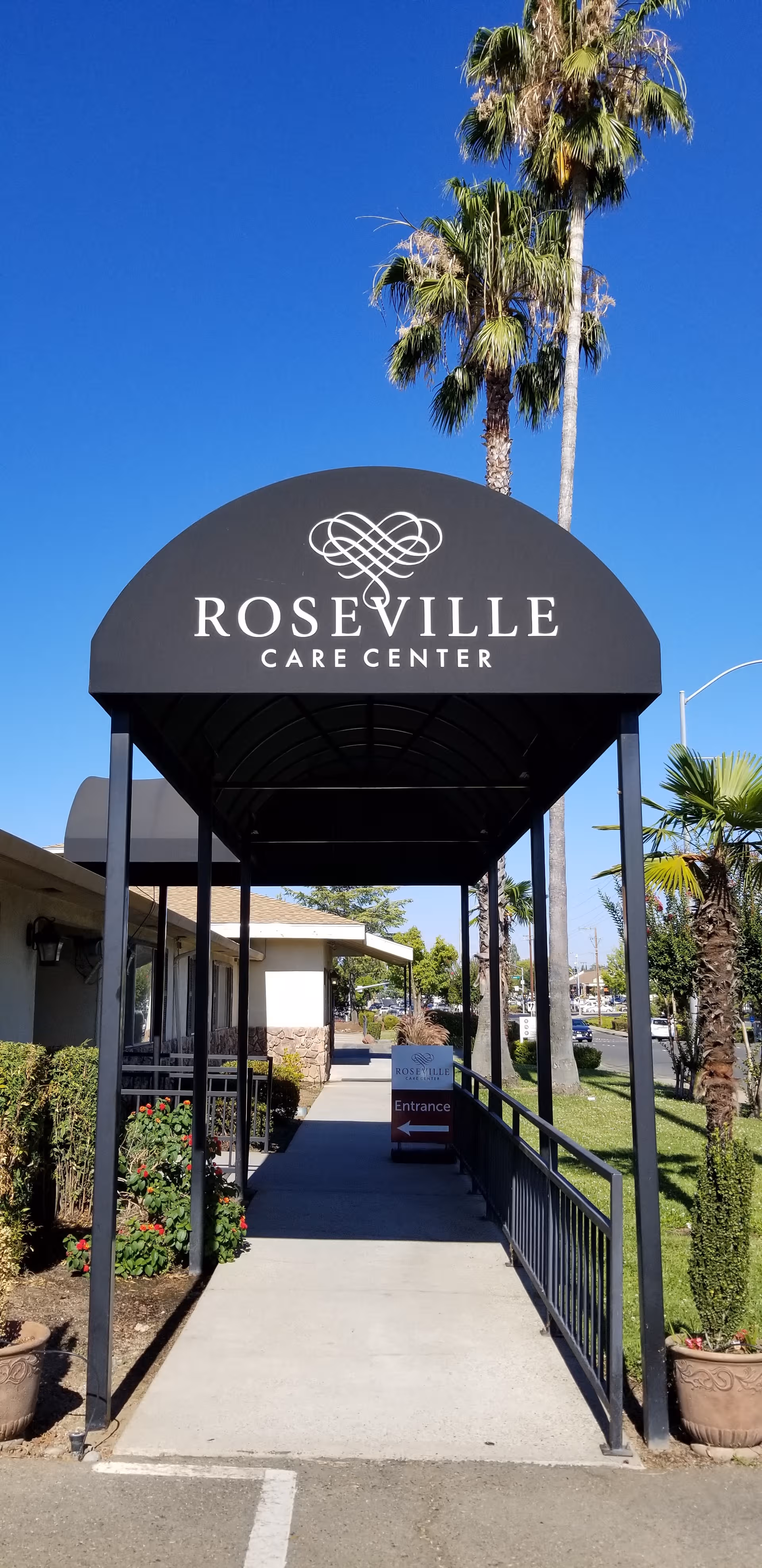 Entrance canopy displays Roseville Care Center with walkway, railing, and palm trees.