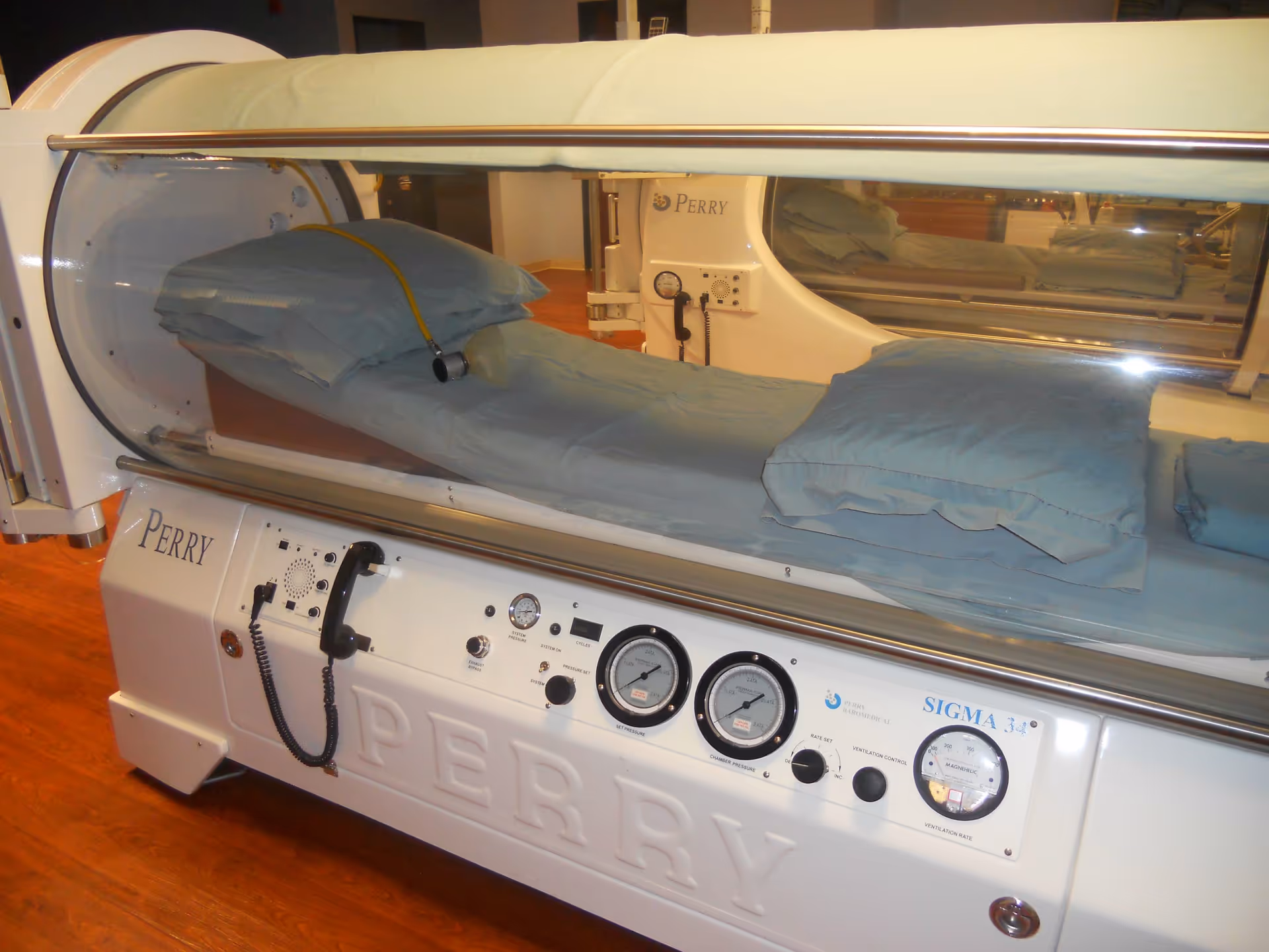 Hyperbaric chamber labeled Perry in a clinical interior with blue cushions.