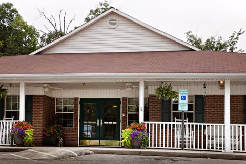 Exterior view of North Pointe of Archdale facility with brick entrance, white porch, and planters.