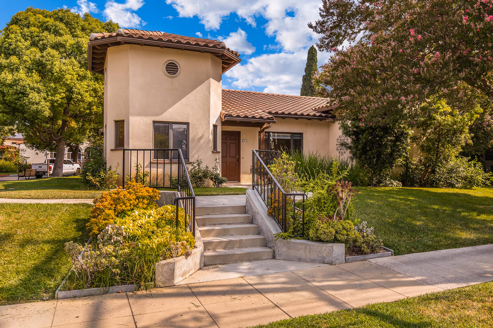 Front exterior of a single-story stucco building with a tiled roof, entrance steps and landscaped lawn.
