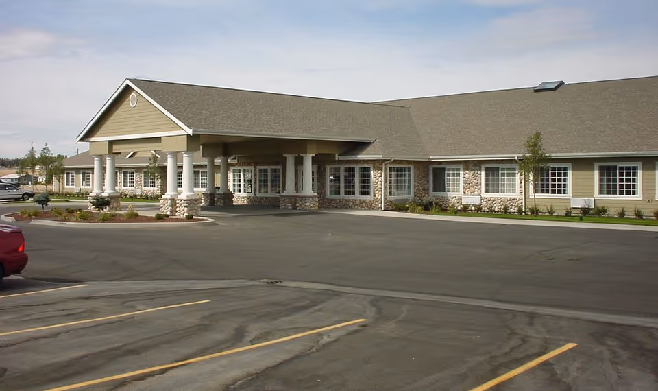 Exterior view of a single-story senior care building with a covered entrance supported by columns and an adjacent parking lot.