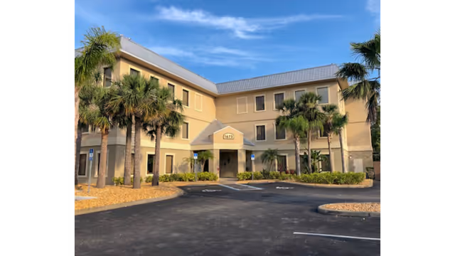 Exterior view of a beige, multi-story facility with palm trees and a welcoming entrance.