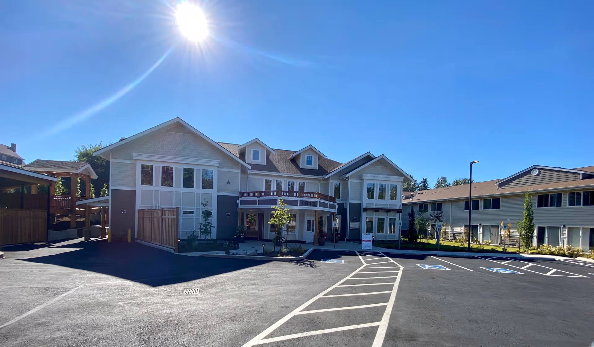 Sunlit senior living facility exterior with a large multi-unit building and parking lot.
