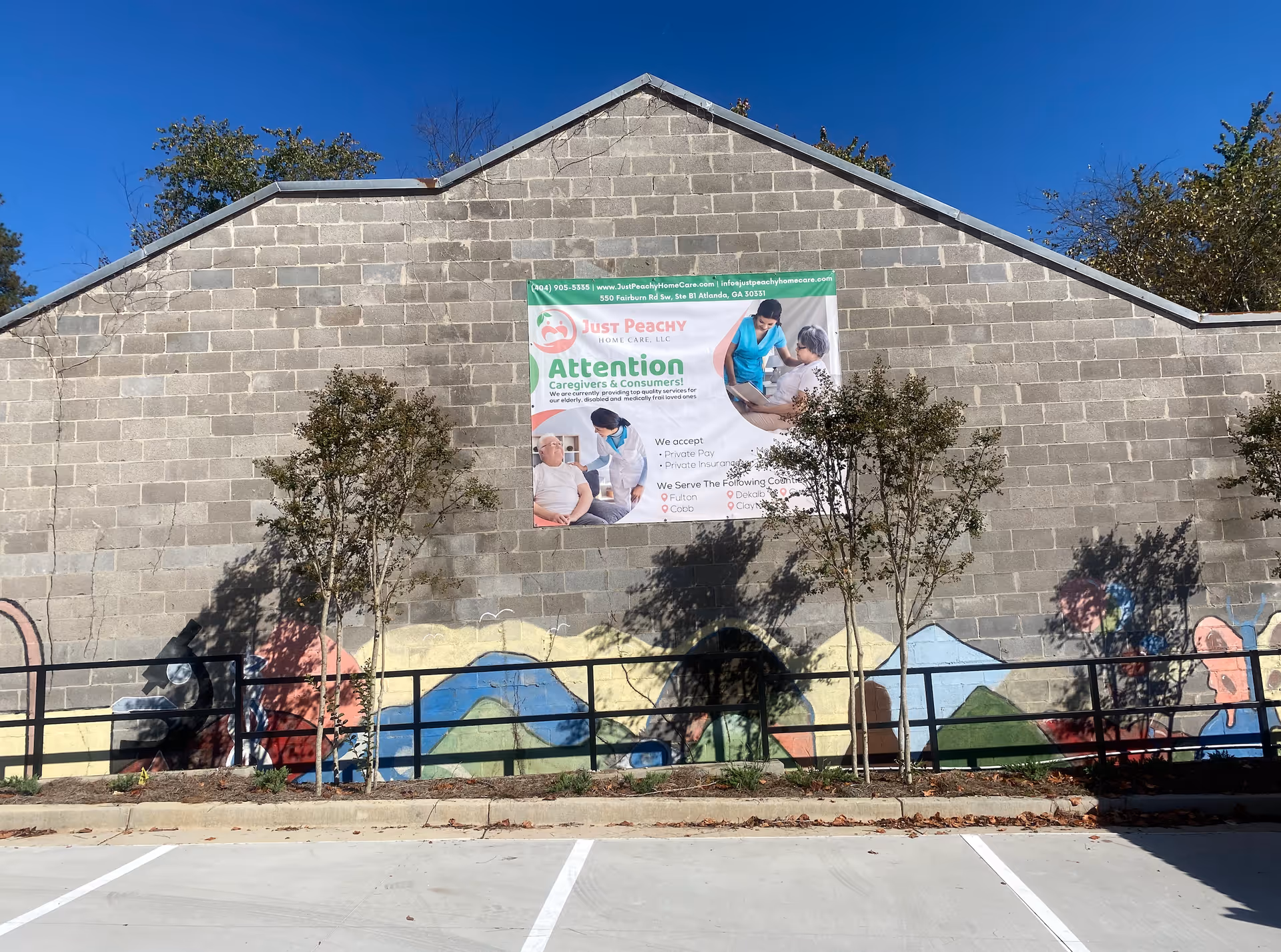 A gray brick wall with a Just Peachy Home Care banner and mural along the exterior.