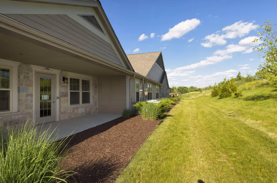 Sunrise Meadows Senior Living building front with lawn, shrubs, and blue sky.