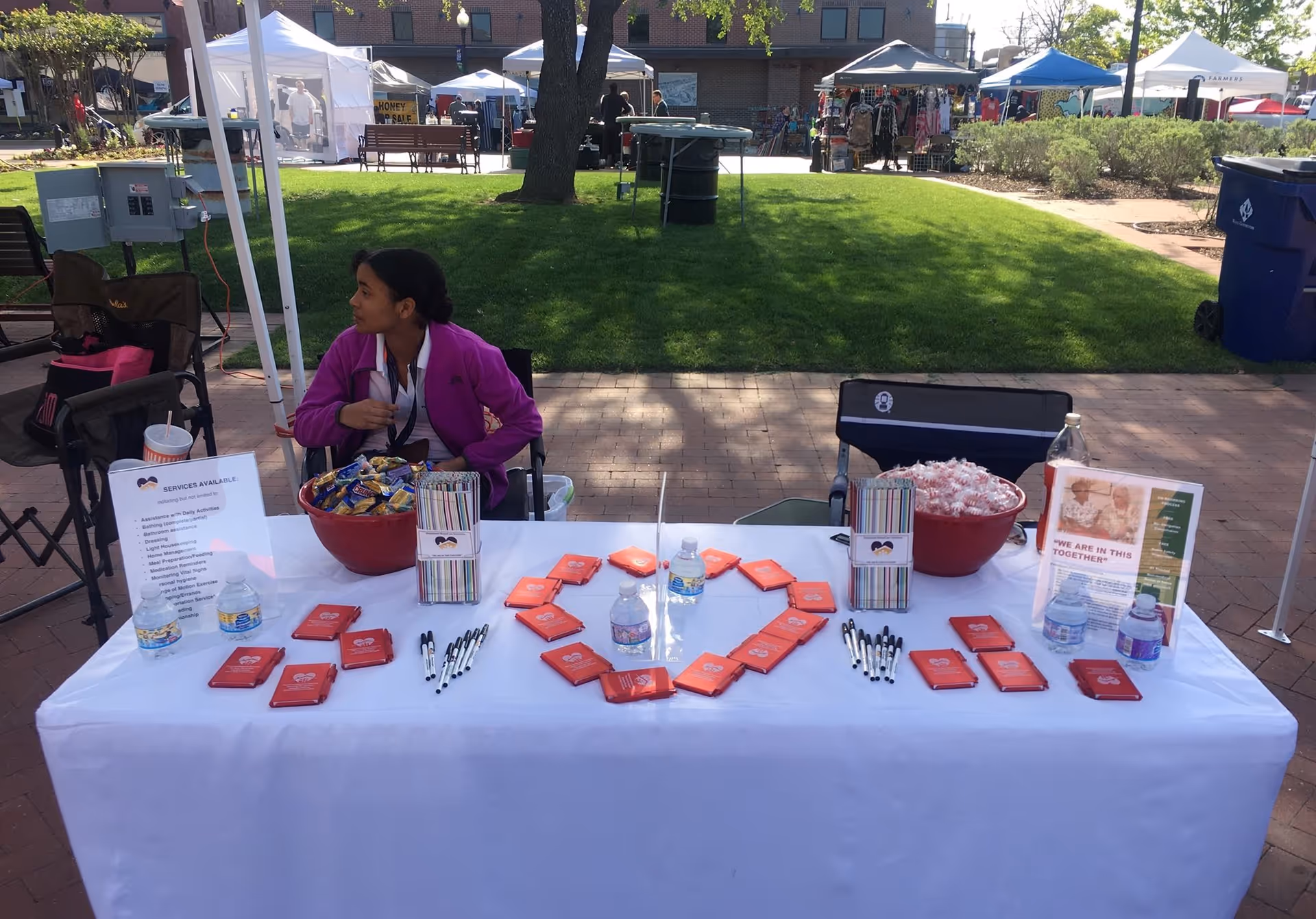 A person sits at an outdoor booth with promotional materials and snack bowls.