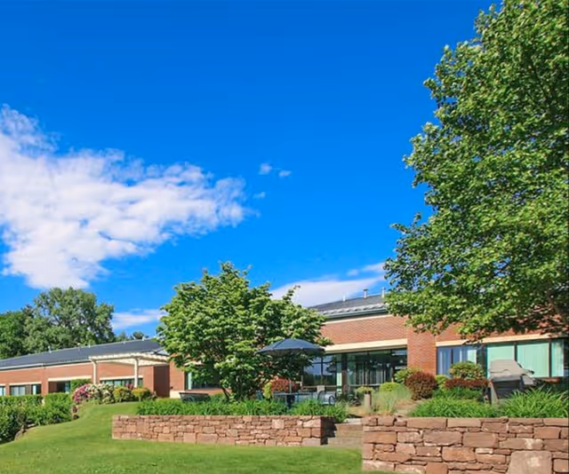 Exterior view of a brick senior living facility with a landscaped lawn and patio.