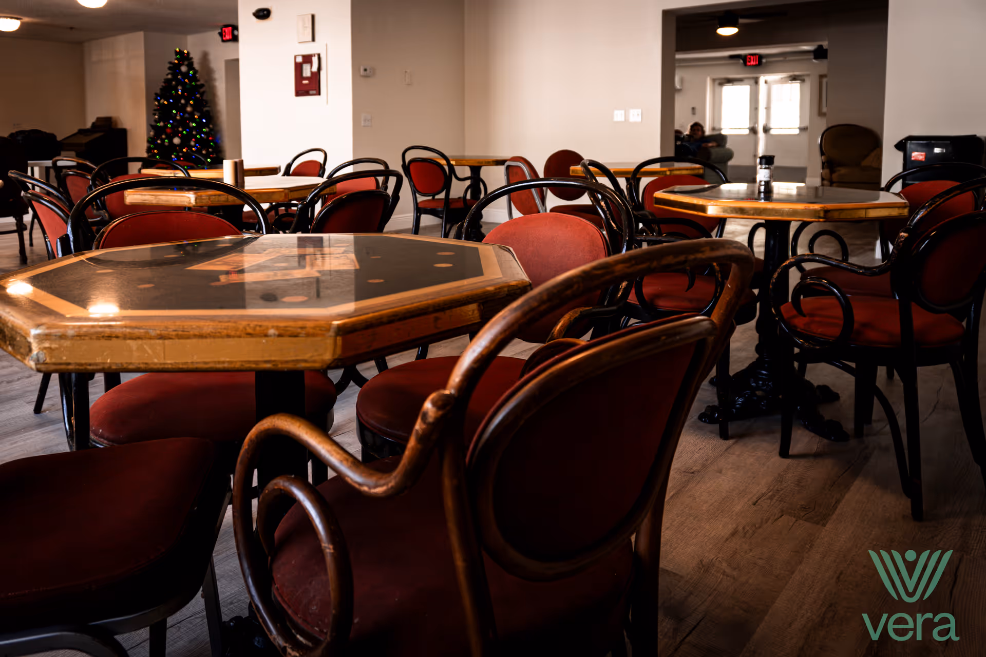 Interior dining room with round tables and red upholstered chairs, Christmas tree in background.