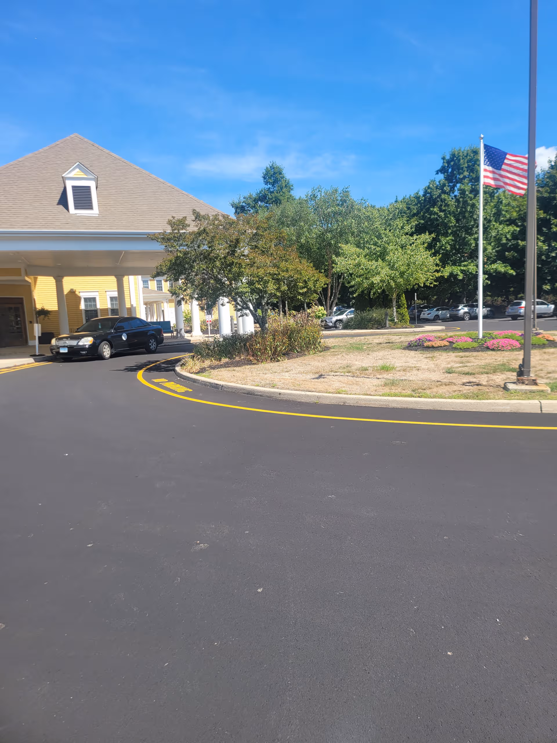 Exterior of Coachman Square at Woodbridge with entrance, circular driveway, trees, and flagpole.