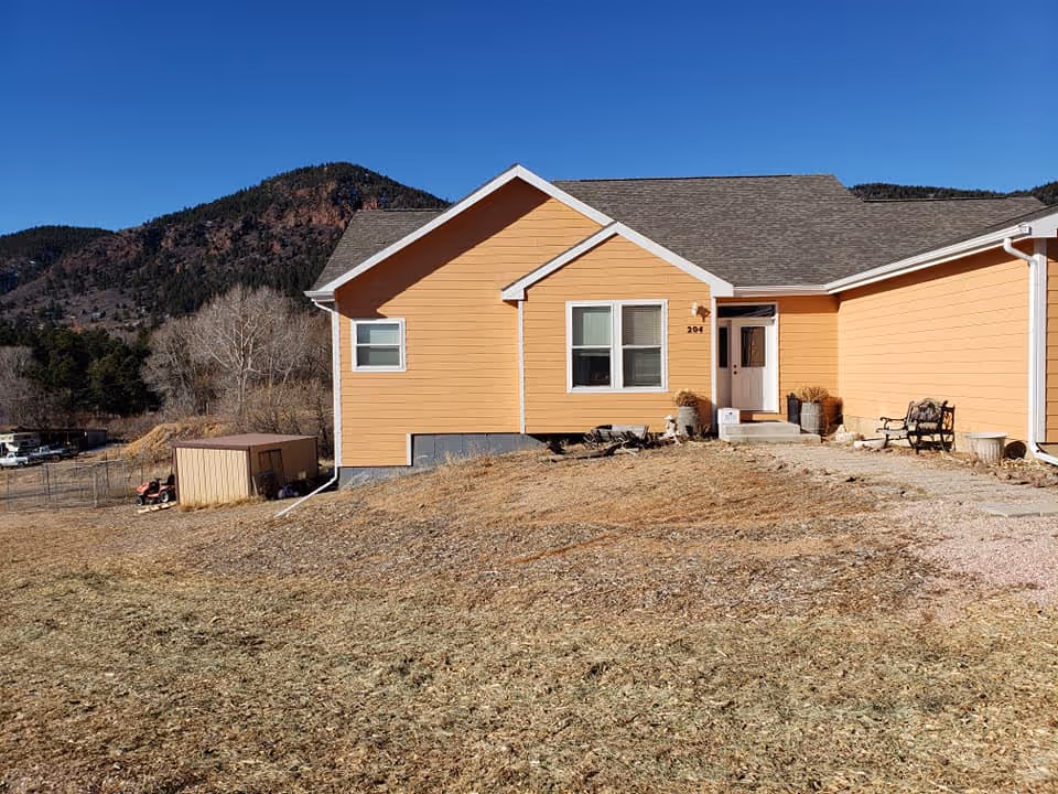 Orange, single-story building with front door, porch seating, and mountain backdrop.