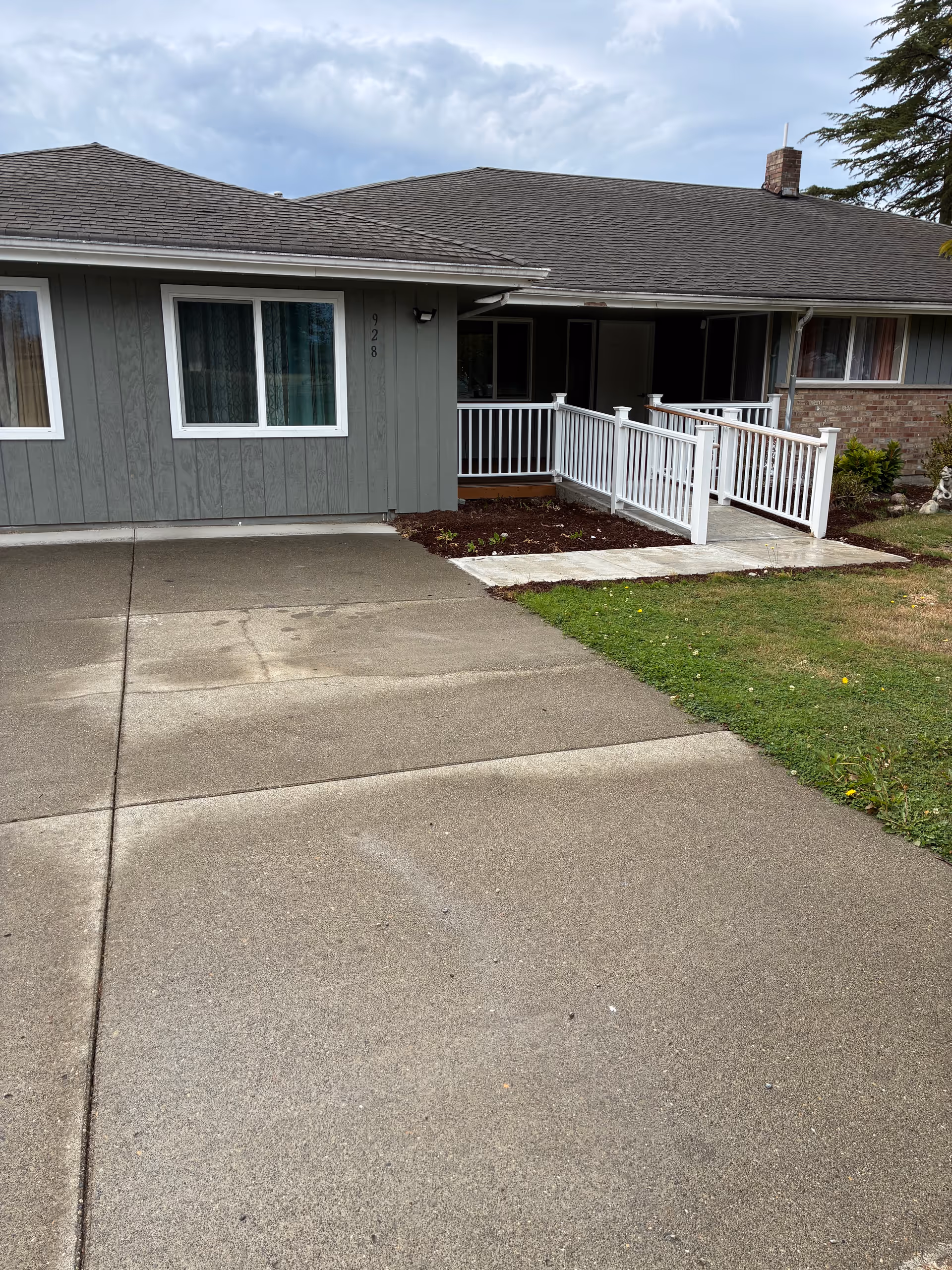 Single-story gray senior living entrance with white railing and concrete walkway leading to door.