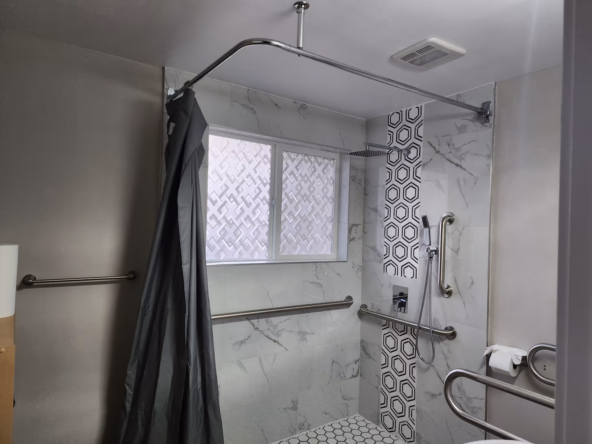 Accessible bathroom with a tiled shower, multiple grab bars, and a hanging curtain.