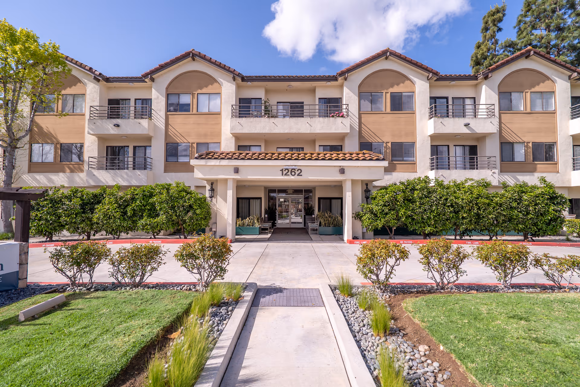 Front view of a tan, three-story senior living building with balconies and entrance.