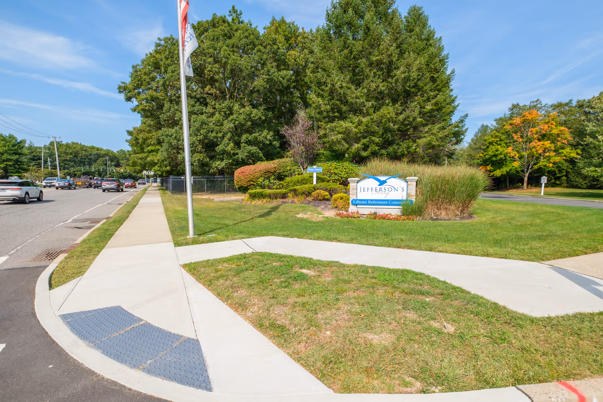 Landscaped sidewalk and entrance sign for Jefferson's Lifecare Retirement Community beside a flagpole.