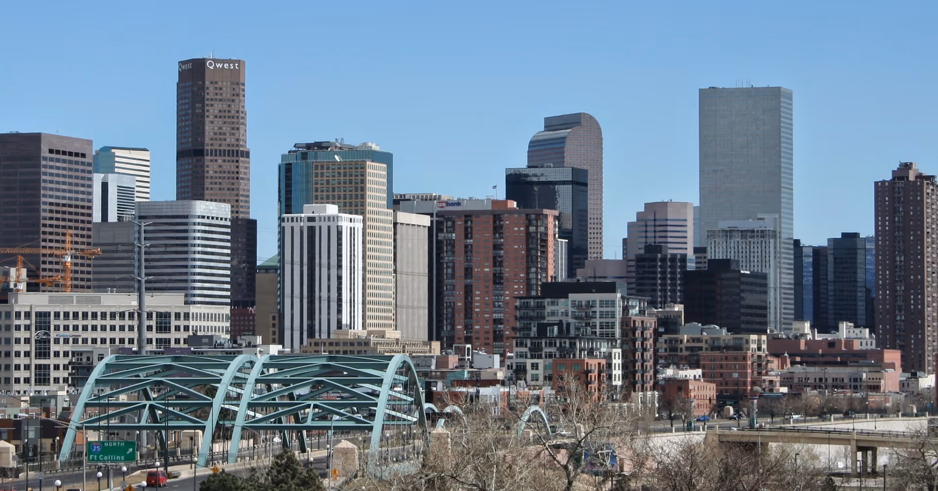 City skyline with tall skyscrapers and teal arched bridge in foreground.