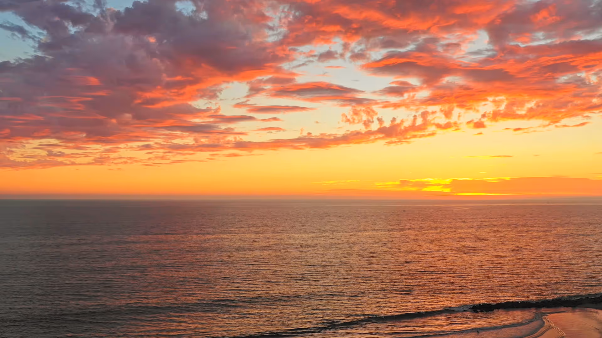 Ocean horizon at sunset with orange and pink clouds over calm water.