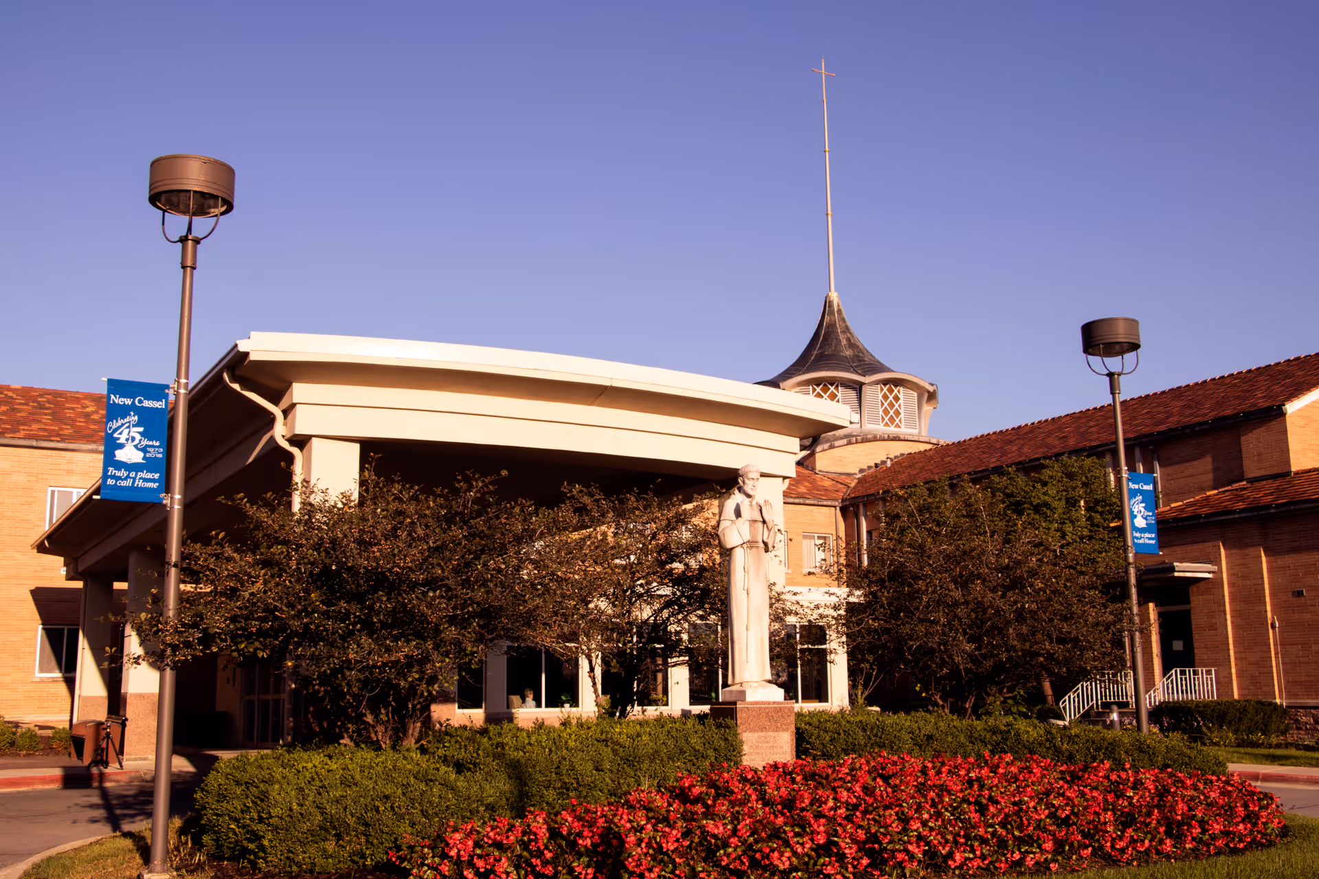 Exterior view of New Cassel Retirement Center with statue, landscaping, and banners.