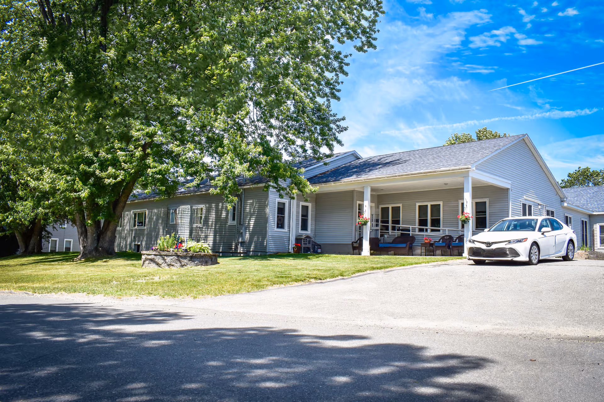 Hilltop Manor senior living facility with a front porch, seating, a parked white car, and trees.