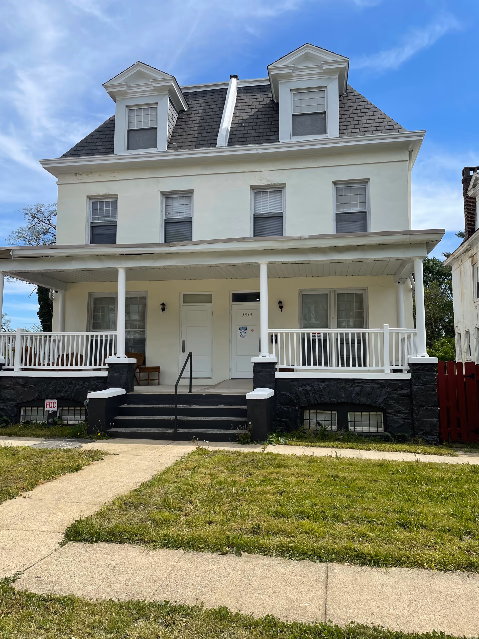 White, two-story building with a covered front porch and black stone foundation.