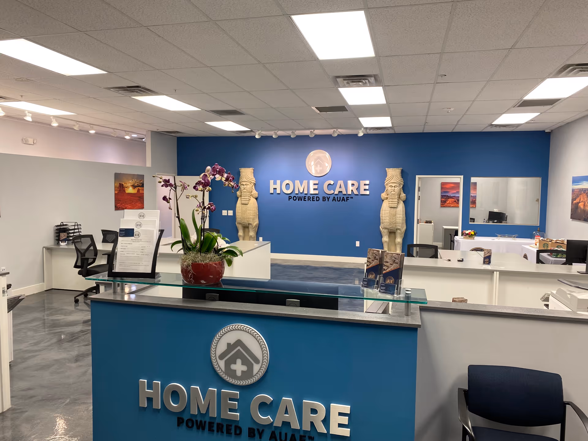 Reception lobby of Home Care Arizona with blue wall logo, statues, and front desk.
