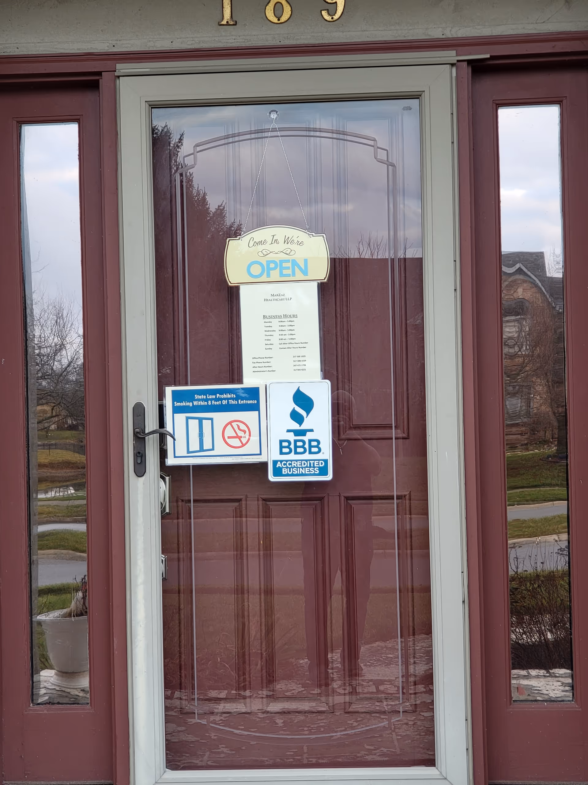 Glass front door with OPEN sign and BBB accreditation stickers on a maroon frame