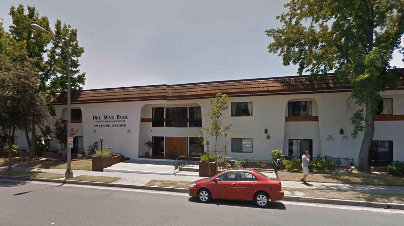 Del Mar Park senior living facility building exterior with sign, sidewalk, trees, and a red car.