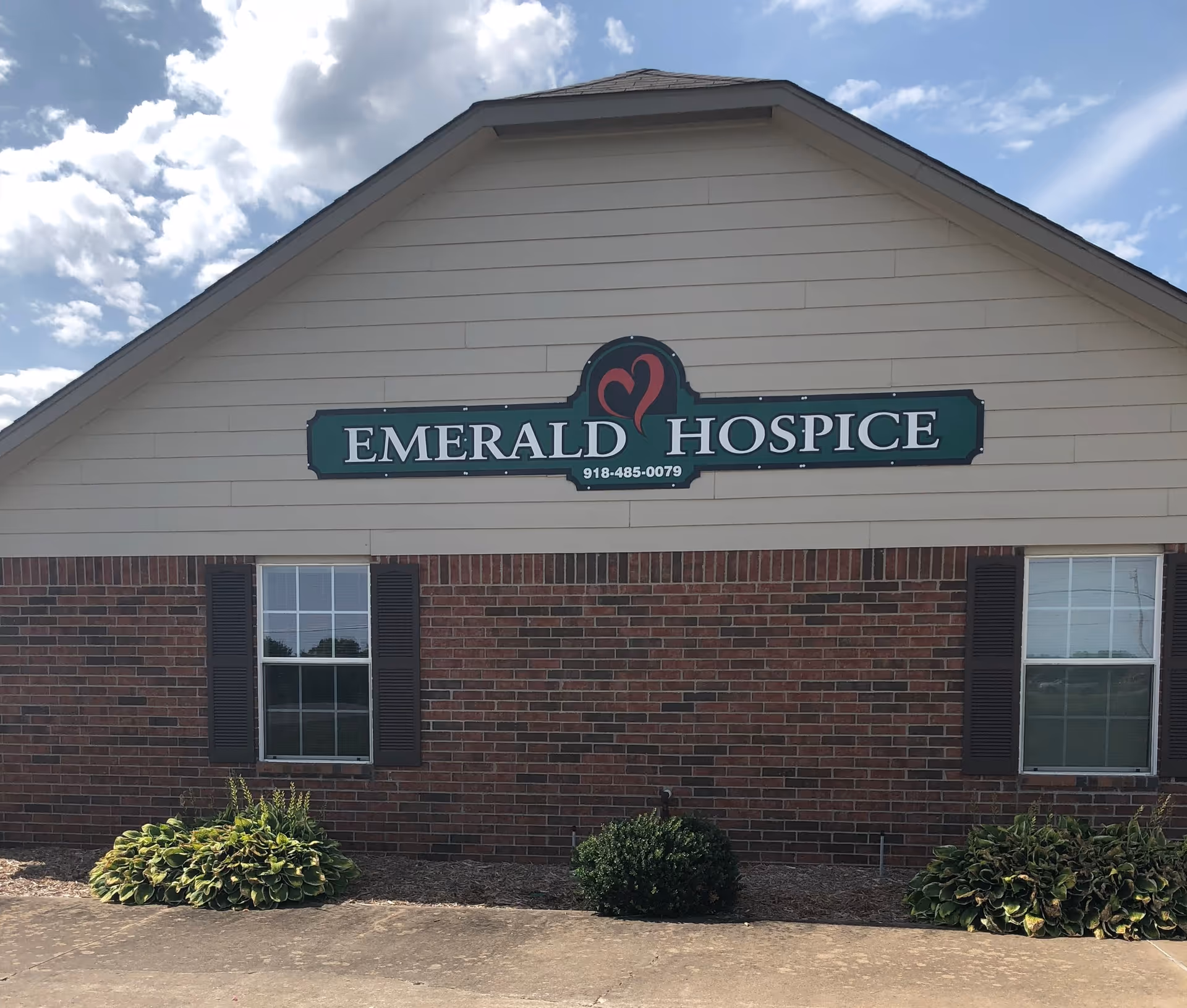 Front exterior of a beige building with an Emerald Hospice sign and landscaping.