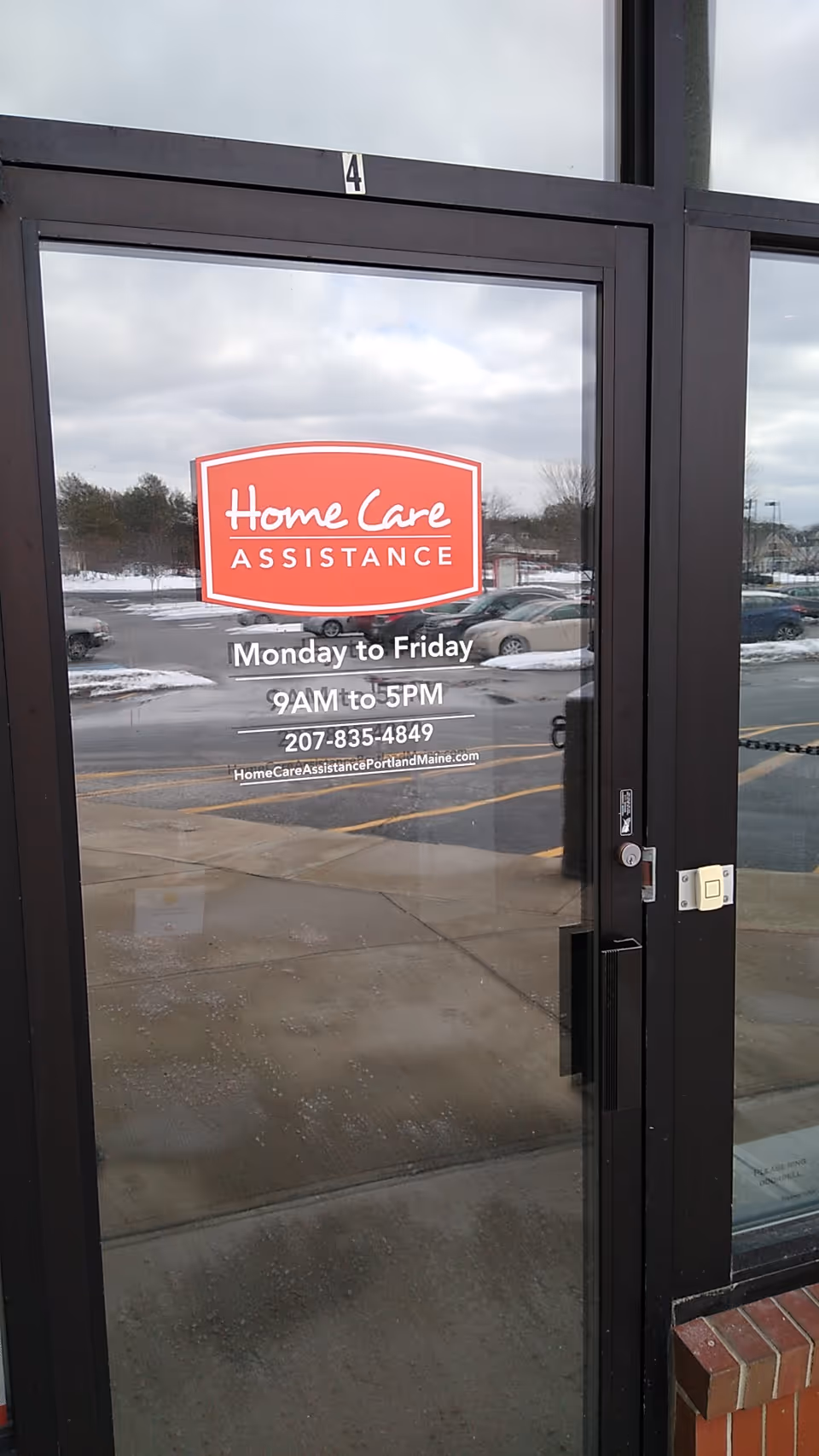 Glass entrance door displaying Home Care Assistance sign, with parking lot visible outside.