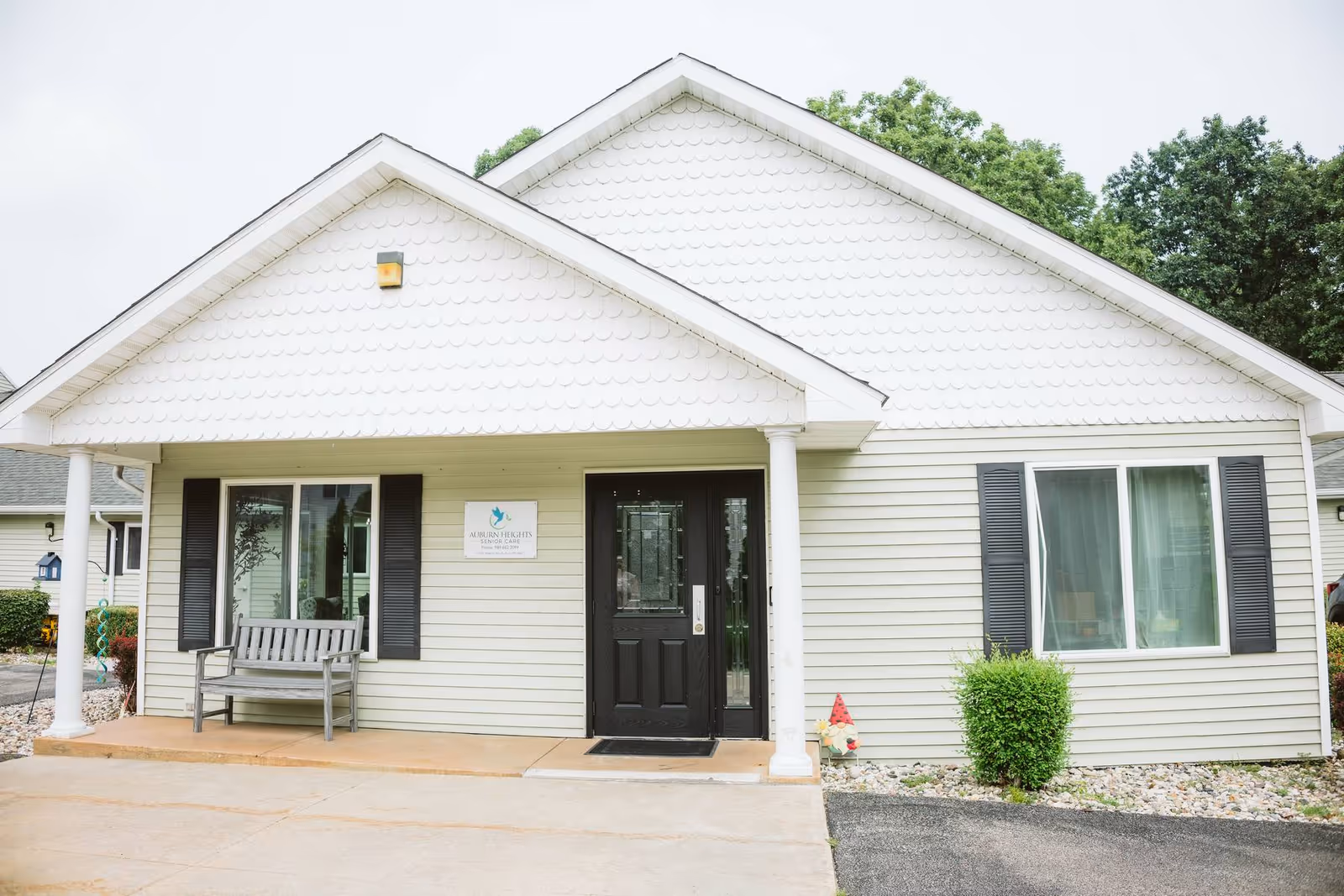 Front view of Auburn Heights Senior Care building with porch, bench, and shrubs.