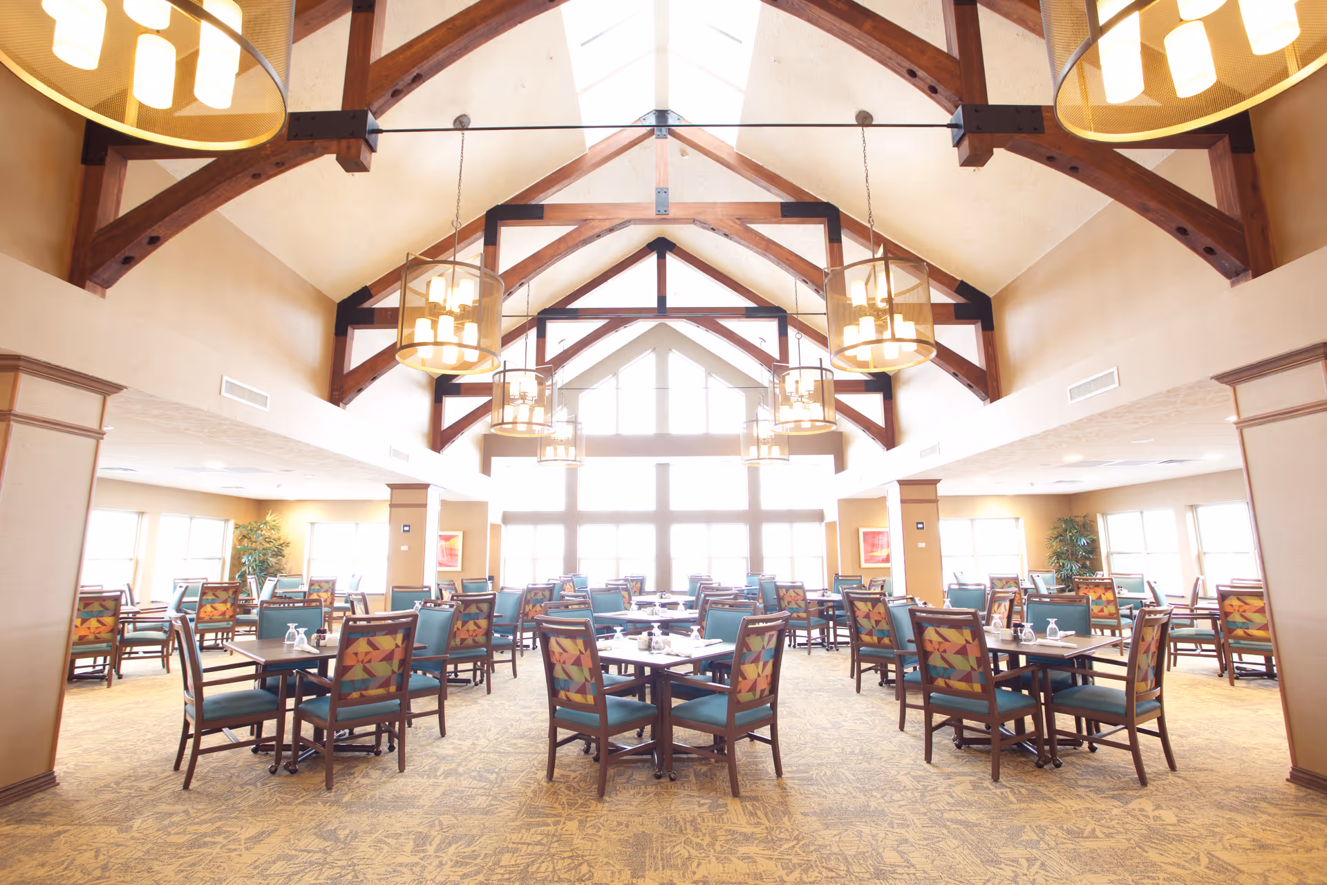 Bright dining hall with vaulted timber beams, large windows, and many arranged tables.